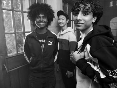 three boys standing in the front hall of their school with backpacks, smiling at the camera. 